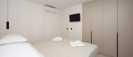 A bedroom with a bed, two pillows, a flat-screen TV, a wardrobe, and a ceiling light fixture.