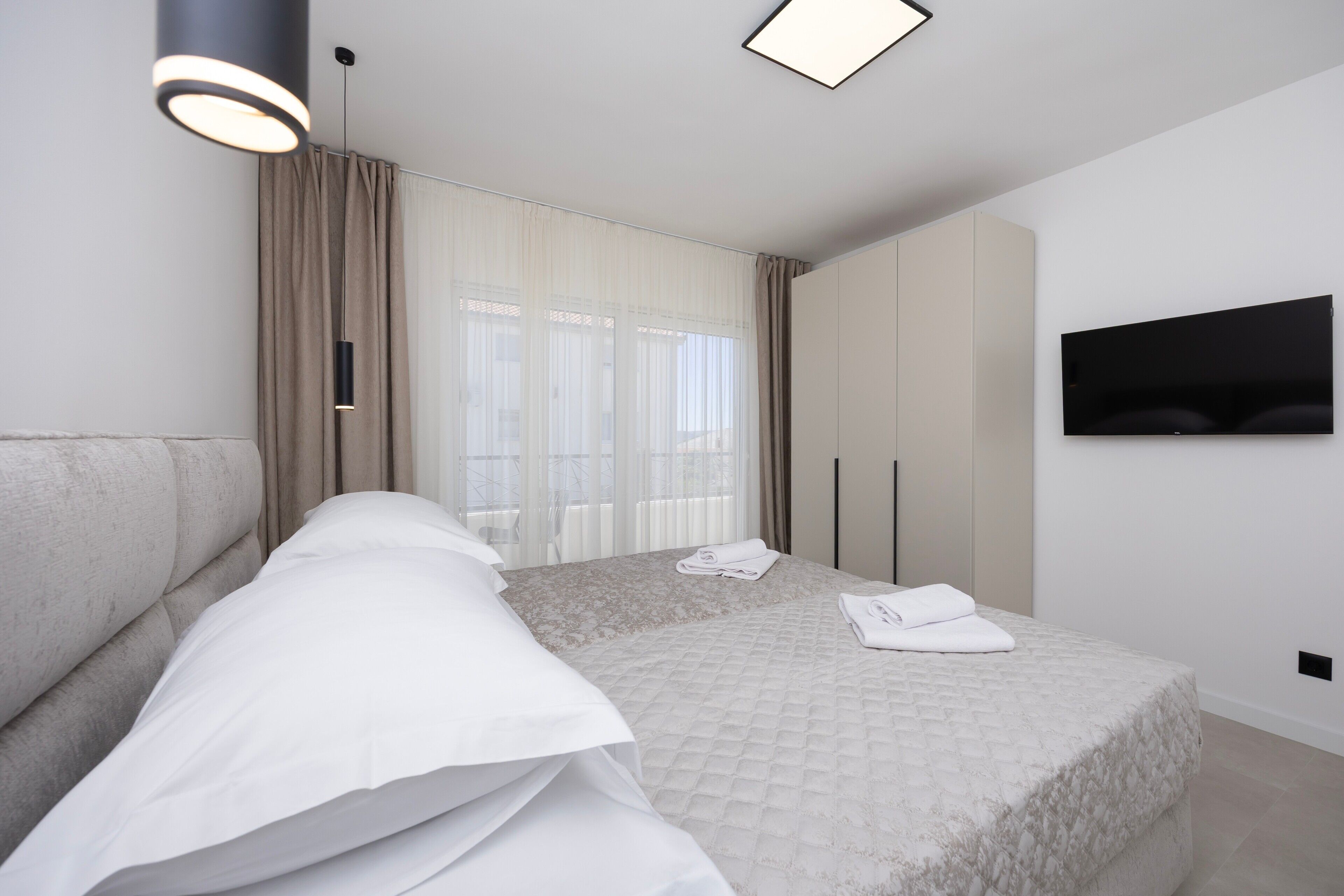 A modern hotel room with a large bed, a flat-screen TV, and a large window with curtains.