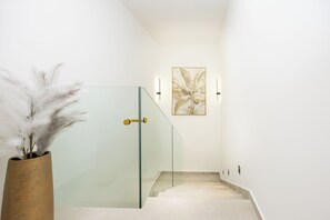 Ein modernes Interieur mit einer gläsernen Treppe, einer Zierpflanze und einem an der Wand befestigten Kunstwerk.
