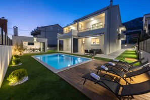 Ein modernes, zweistöckiges Haus mit Swimmingpool, Gartenmöbeln und einem gepflegten Rasen.
