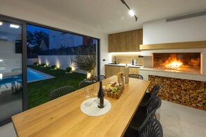 Eine moderne Küche mit integriertem Kamin, einem Essbereich mit Holztisch und Blick auf einen Swimmingpool.