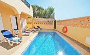 Piscina con sillas de descanso y un flotador salvavidas, rodeada por un muro de piedra y una valla decorativa.
