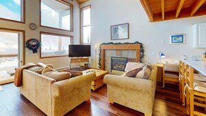 A cozy living room with a fireplace, large windows, and a television.