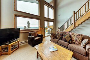 A living room with a large TV, a sofa, a coffee table, and a staircase. - Arolla Chalet by Okanagan Premier (Beaverdell)