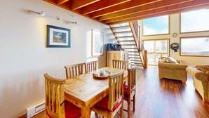 A wooden dining table with chairs, a sofa, and a staircase leading to a balcony.