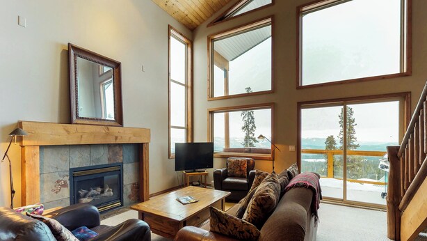 A spacious living room with a fireplace, leather sofas, a television, and large windows offering a view of the outdoors.