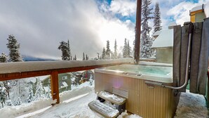 A hot tub with steps leading up to it, surrounded by snow-covered trees and a wooden deck.
