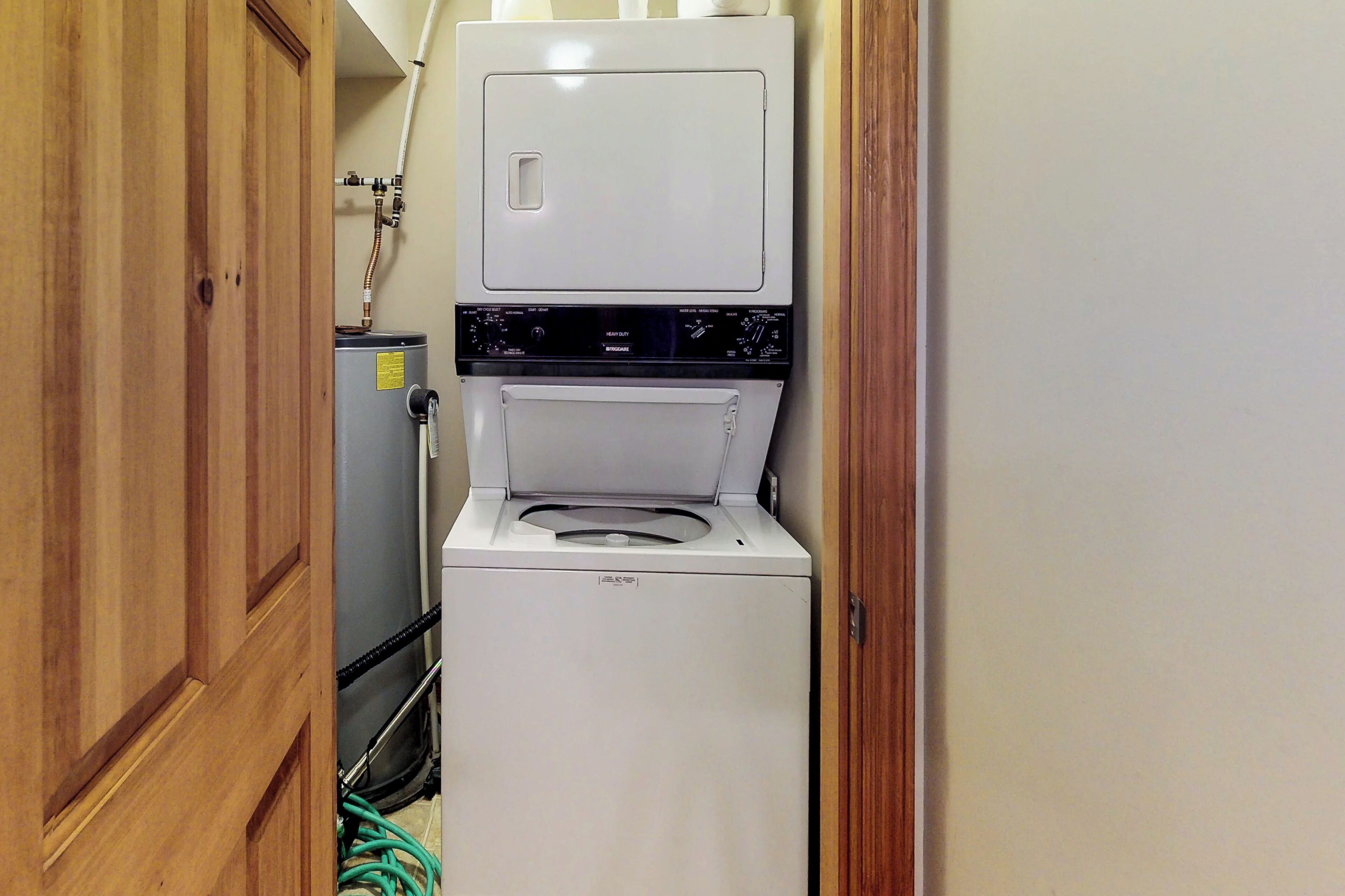A compact laundry room with a front-loading washer and dryer, a water heater, and a wooden door.