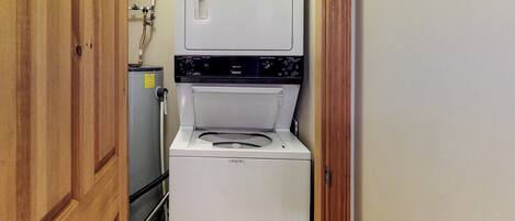 A compact laundry room with a front-loading washer and dryer, a water heater, and a wooden door.