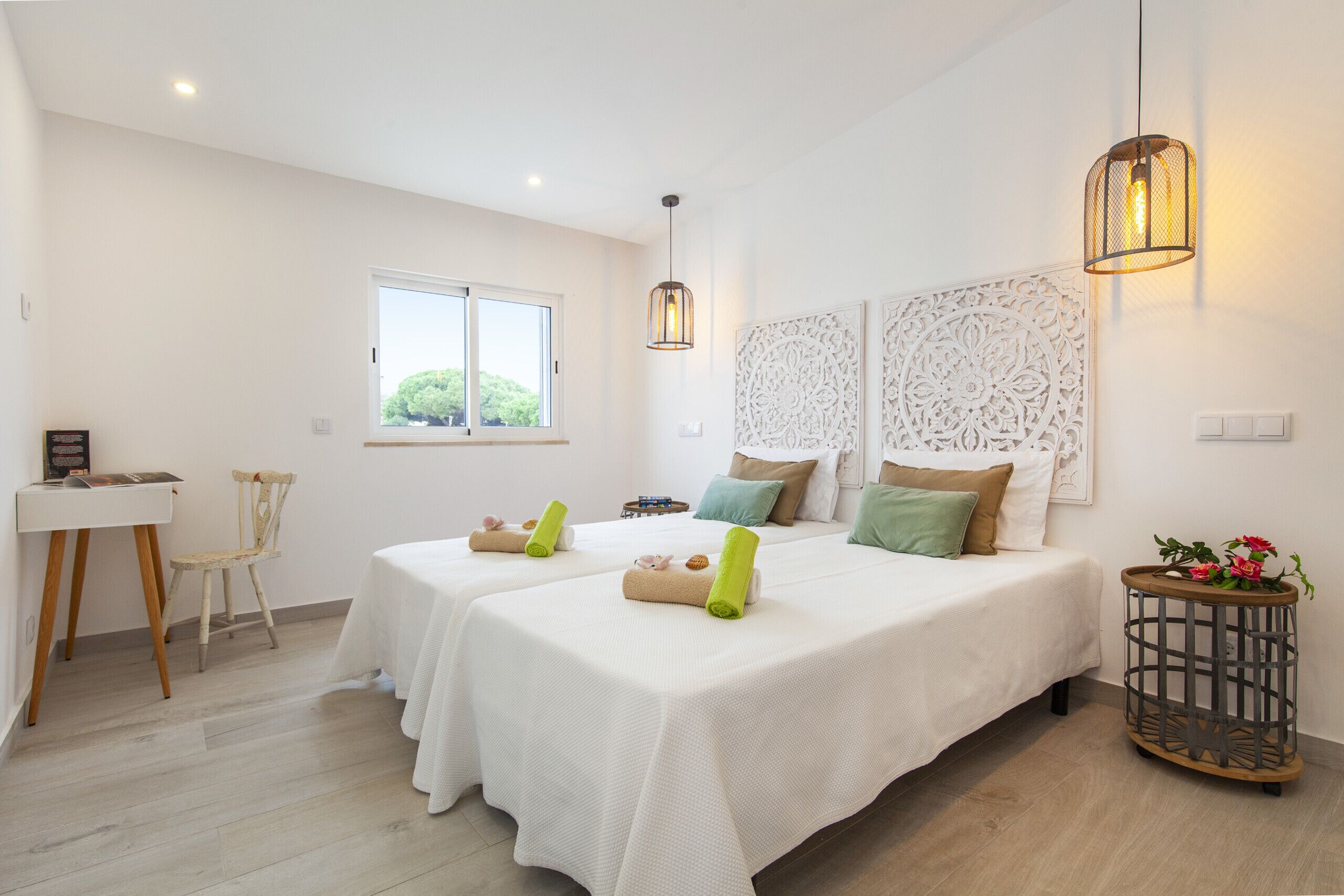 A hotel room with two beds, a desk, a chair, a window, and decorative wall panels.