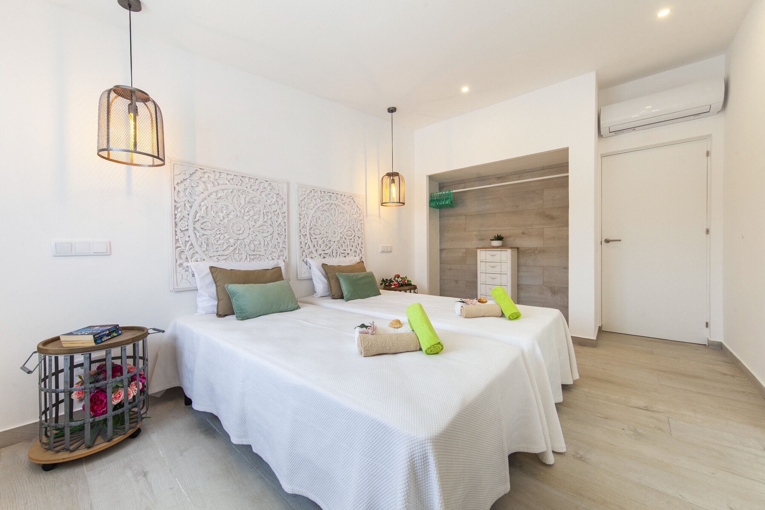 Un dormitori modern amb dos llits, una taula auxiliar petita, un panell decoratiu a la paret i un llum penjant.