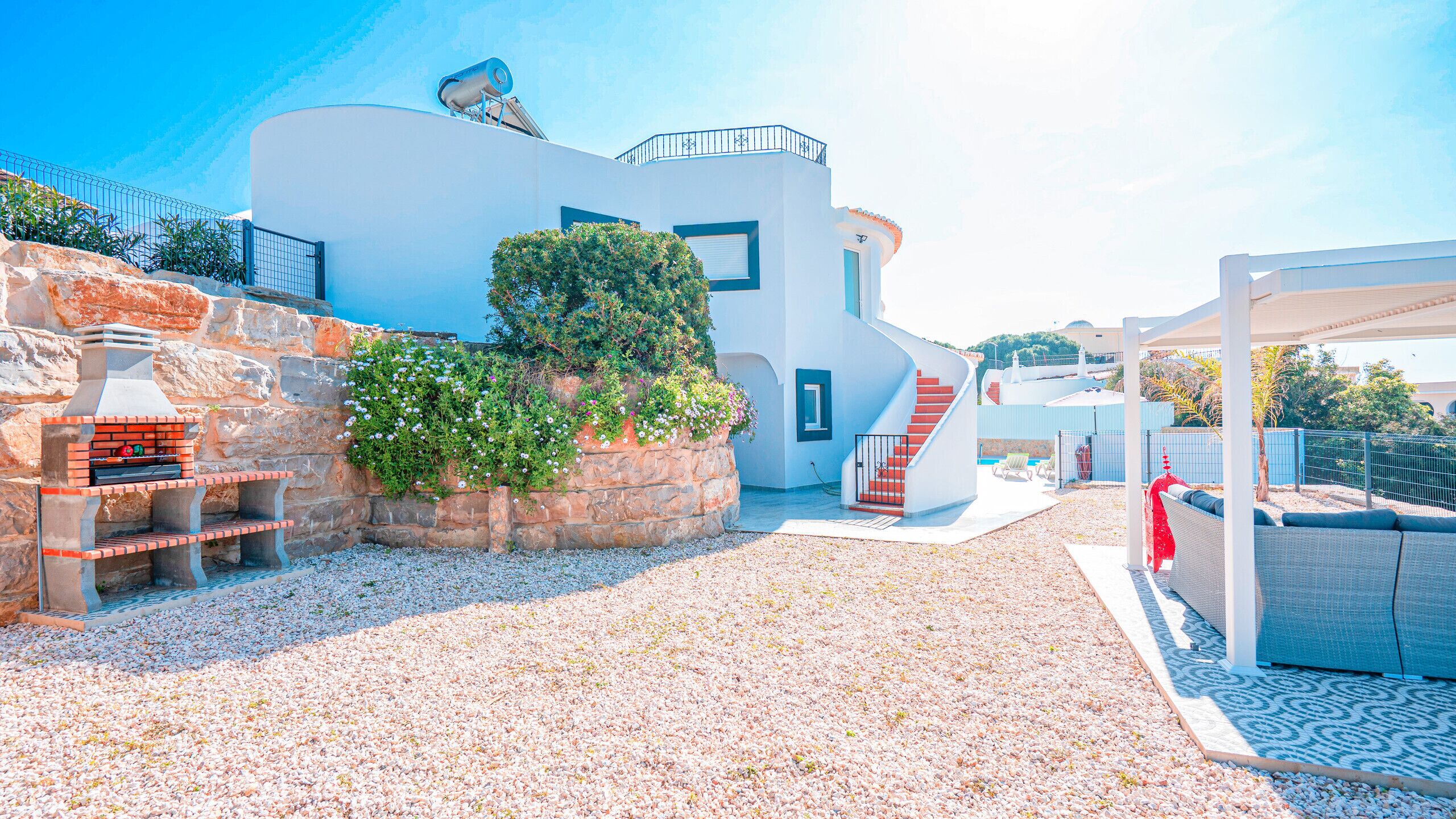 Una vila moderna amb mur de pedra, zona de barbacoa i zona d'estar coberta a l'aire lliure.