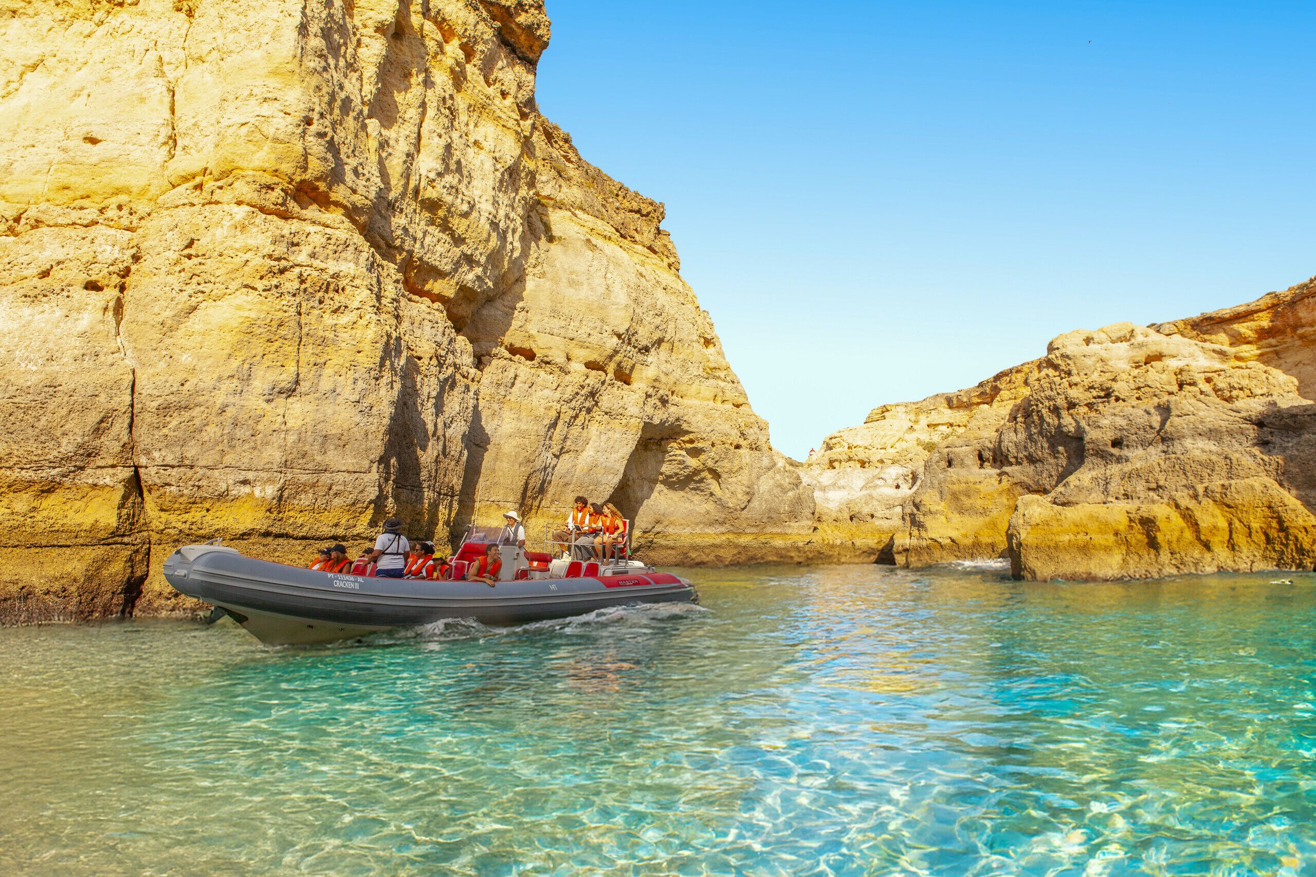 Un barco con pasajeros en un mar turquesa transparente, rodeado de acantilados rocosos.