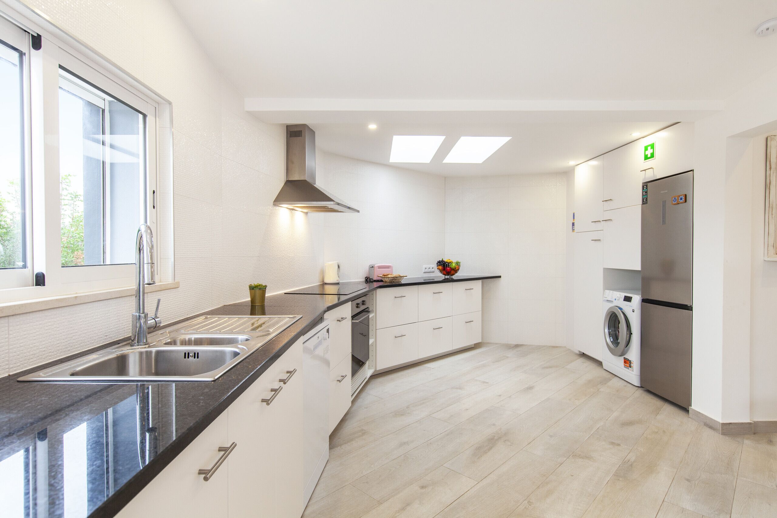 Eine moderne Küche mit Spüle aus Edelstahl, eingebautem Ofen, Waschmaschine und Kühlschrank.