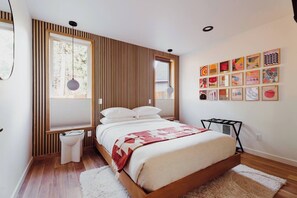 Een moderne slaapkamer met een groot bed, houten paneelwanden, een witte vloer en een wand vol kleurrijke kunstwerken.