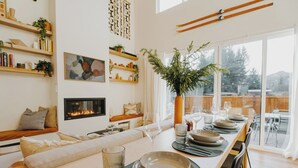 Uma sala de estar moderna com lareira, espaço de jantar para seis pessoas e uma grande janela com vista.