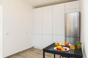 Una cocina moderna con armarios blancos, un refrigerador de acero inoxidable y una mesa de comedor con alimentos para el desayuno.
