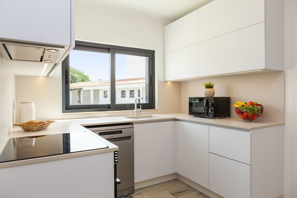 A modern kitchen with white cabinets, a built-in dishwasher, a microwave, and a fruit bowl on the counter. - Villa Solarys (Albufeira)
