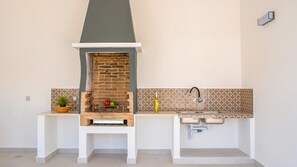 A compact kitchen with a brick oven, a sink, and a decorative backsplash. - Villa Solarys (Albufeira)