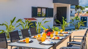 A dining table set outdoors with chairs, a fruit basket, and a pitcher of orange juice. - Villa Solarys (Albufeira)