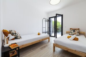 A modern bedroom with two single beds, a wooden nightstand, a reading lamp, and a window with a view of greenery. - Villa Solarys (Albufeira)