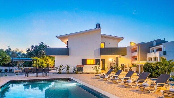 Un hôtel moderne doté d’une piscine, de chaises longues et d’un espace extérieur aménagé et abrité.