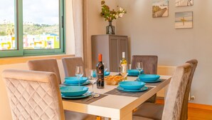 Une table à manger dressée avec de l’argenterie bleue, des verres à vin et une bouteille de vin, avec vue sur les bâtiments à travers la fenêtre.