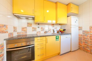 Una cocina con gabinetes amarillos, horno de acero inoxidable, refrigerador blanco y un lavabo.