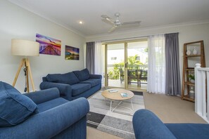 Ein Wohnzimmer mit einer Couch, einem Couchtisch, einer Lampe, einem Deckenventilator und Blick ins Freie.