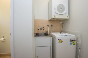 Een kleine wasruimte met een wasmachine, een spoelbak en een wandgedroogde wasdroger.