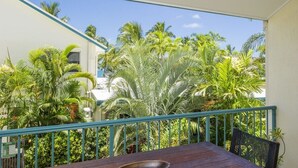 A balcony with a table and chairs, surrounded by lush tropical plants and a clear blue sky.