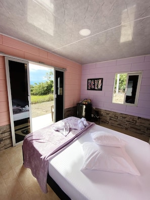 Una habitación con una cama, una puerta corredera a un balcón, una mesita y un cuadro en la pared.