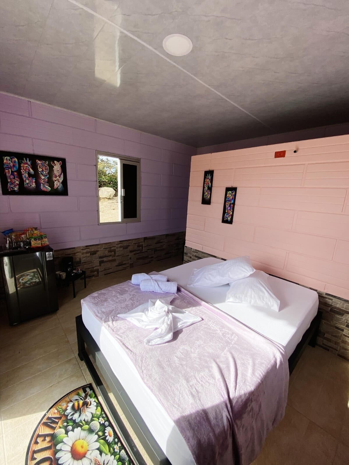 Une chambre avec deux lits, une petite kitchenette, une fenêtre et un mur décoré d’œuvres d’art.