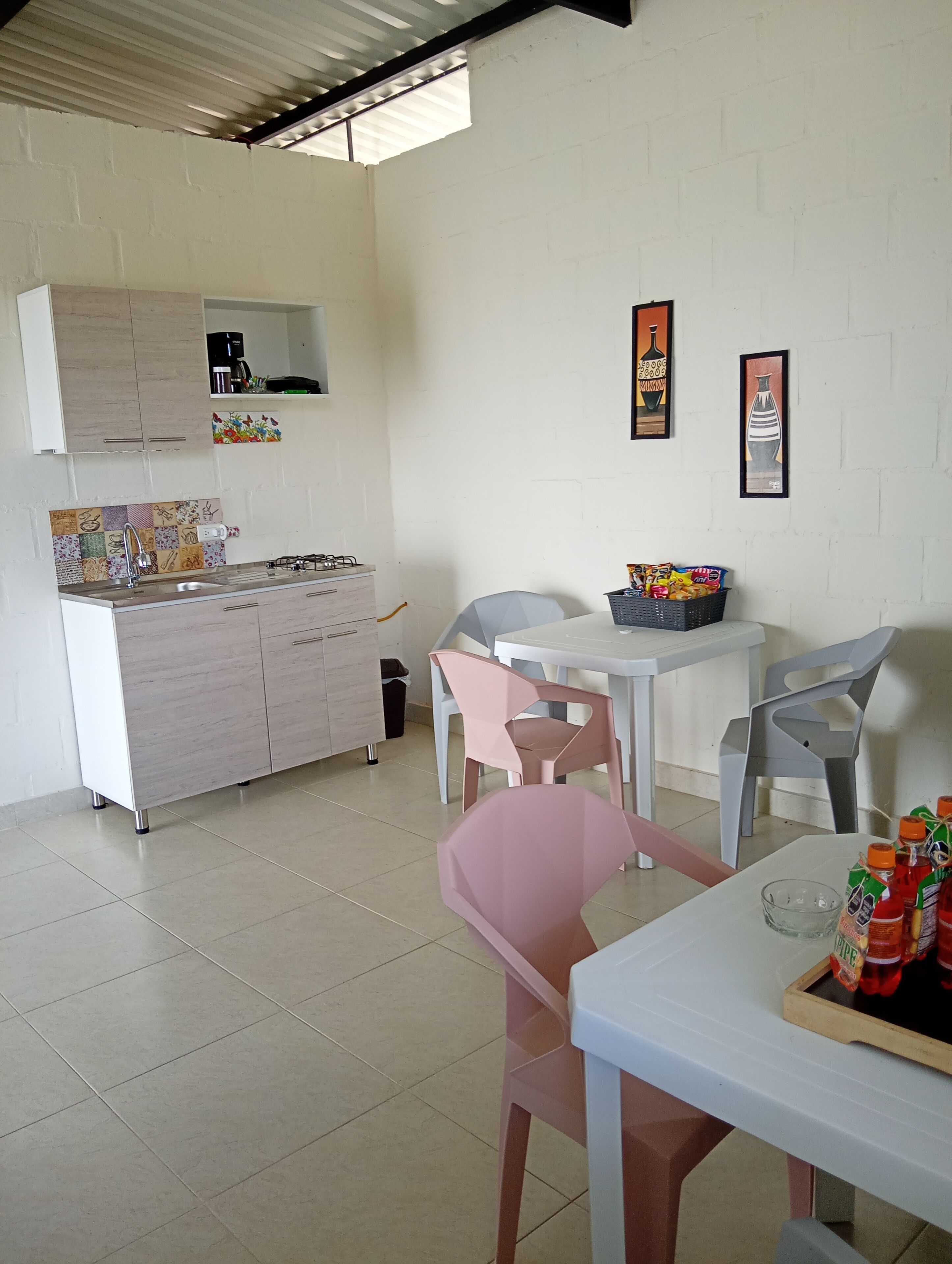 A compact kitchen with a gas stove, sink, and white cabinets. There is a dining area with a table and chairs, and two framed artworks on the wall.