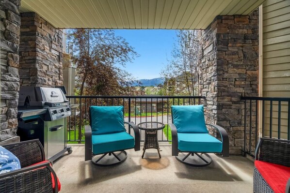 A balcony with stone walls, a grill, two teal chairs, and a small table. - Laguna | Lake | Outdoor Pool/Hot Tub | Gym | Pets (Invermere)