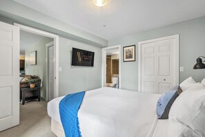 A bedroom with a bed, a desk, a chair, a lamp, and a bathroom visible through an open door. - Laguna | Lake | Outdoor Pool/Hot Tub | Gym | Pets (Invermere)