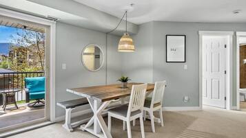 Un coin repas avec une table en bois, des chaises blanches, un luminaire suspendu, un miroir et un tableau encadré au mur.