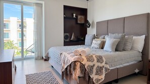 A bedroom with a large bed, a built-in shelf with decorative items, a view of the outside balcony, and a modern headboard. - Luxury Vallarta Marina 1BR Balcony Golf  (Puerto Vallarta)
