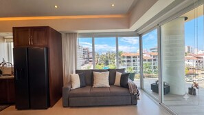 Una sala de estar moderna con sofá, refrigerador y ventanas amplias que ofrecen vista a la ciudad.