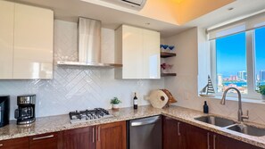 Una cocina moderna con estufa a gas, electrodomésticos de acero inoxidable, armarios de madera y vistas a la ciudad a través de amplios ventanales.