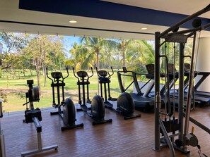 Un gimnasio con diverso equipamiento de ejercicio, vistas a un campo de golf y un ventanal grande.