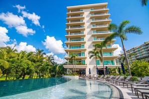 Ein Hotel mit großem Pool, Palmen und wolkenlosem, blauem Himmel.