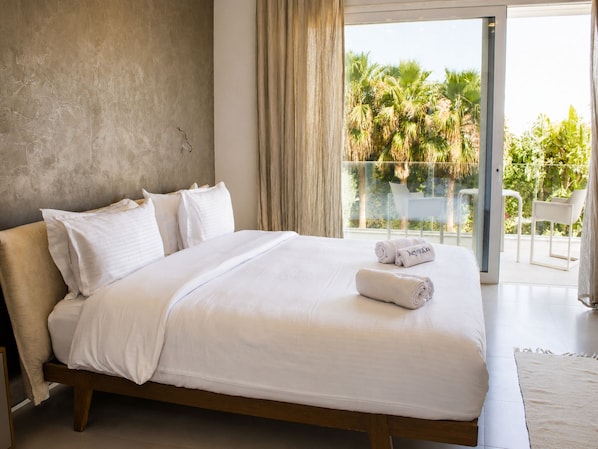 A modern hotel room with a large bed, a balcony with a view of palm trees, and a sliding glass door. - Luxurious Villa Rental in Tunis With Private Indoor Pool (La Soukra)
