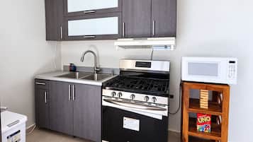 Cocina compacta con estufa, microondas y una pequeña mesa de madera con una caja del juego UNO.