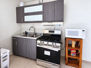 Cocina compacta con estufa, microondas y una pequeña mesa de madera con una caja del juego UNO.