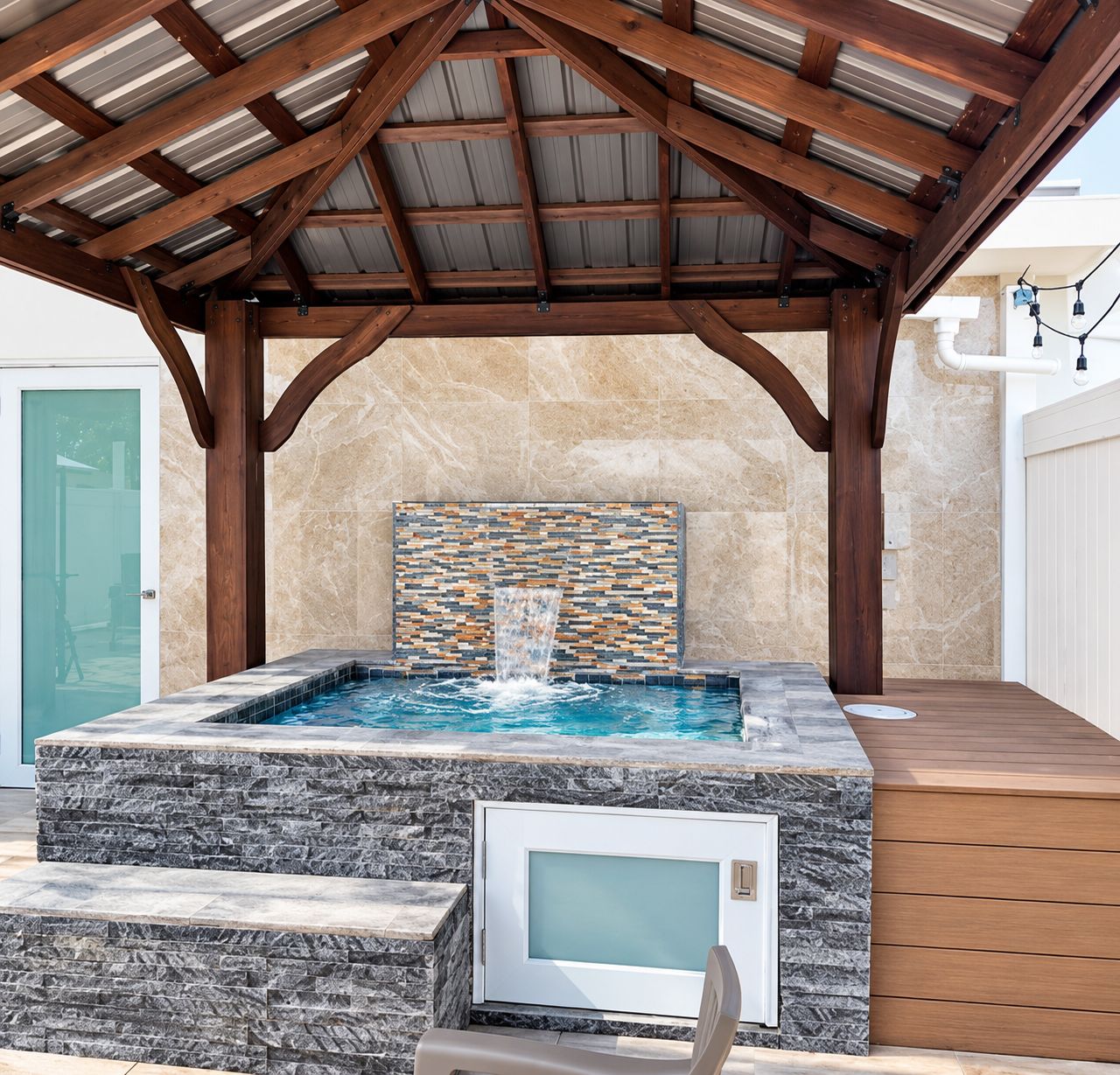 A hot tub under a wooden pergola with a stone wall backdrop.