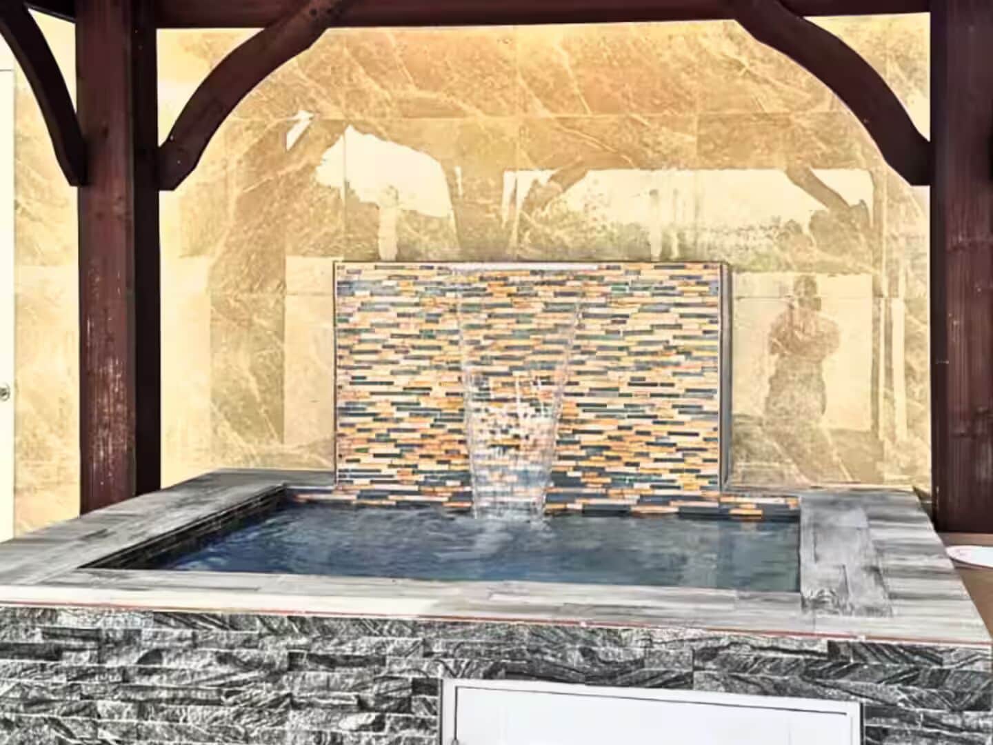 A hot tub with a mosaic wall and stone flooring.