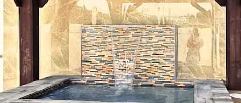 A hot tub with a mosaic wall and stone flooring.