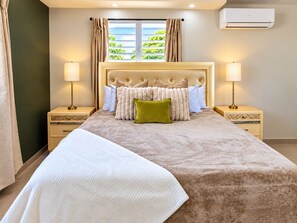 Habitación de hotel con una cama grande, dos mesitas de noche, una ventana con cortinas y un equipo de aire acondicionado en la pared.