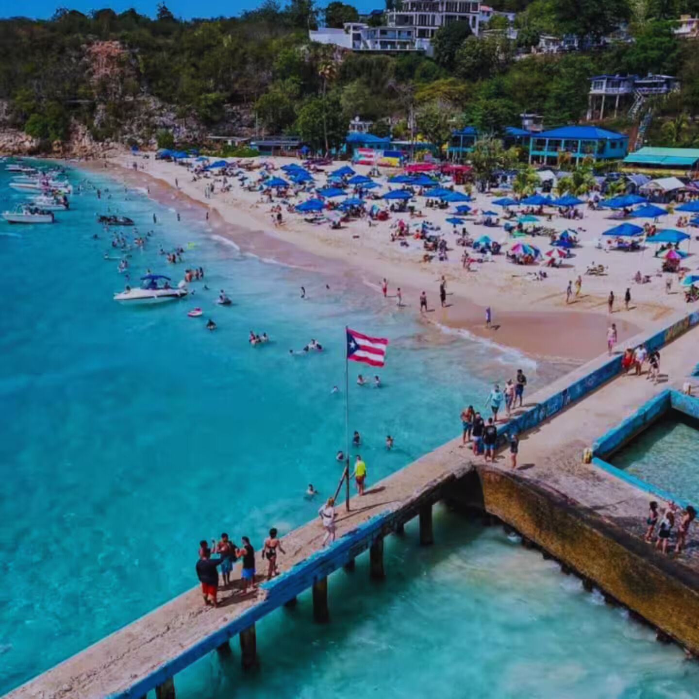 Una playa con muelle, agua turquesa cristalina y una bandera.